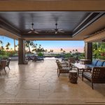 Outdoor seating area of a luxury villa with tropical garden views and a sunset over the ocean in the distance.