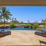 Outdoor terrace with lounge chairs overlooking a pool, tropical garden, and ocean view with palm trees.
