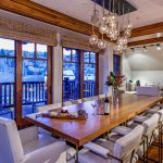 Dining area in a luxury villa with a wooden table, modern chairs, decorative lighting, and large windows overlooking a scenic view.