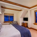 Bedroom interior in a luxury villa with a large bed, nightstand, armchair, and TV, featuring wooden accents and nighttime window views.