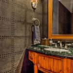 Bathroom with dark patterned walls, a wooden vanity with a marble countertop, a mirror with a wooden frame, and various toiletries.