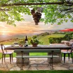 Outdoor dining area with a stone table, wine and glasses, overlooking a vineyard and sunset.
