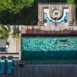 Aerial view of a luxury villa with a swimming pool, sun loungers, and a seating area surrounded by lush greenery.
