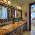 Elegant bathroom interior with double sinks, ornate mirrors, and warm lighting, leading into a cozy bedroom with a comfy bed and nightstand.