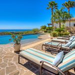 Luxury villa patio with pool and ocean view, featuring lounge chairs and tropical landscaping.
