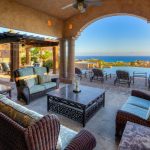 Spacious outdoor patio of a luxury villa with ocean views in Los Cabos, featuring comfortable seating, a dining area under a pergola, and an infinity pool.
